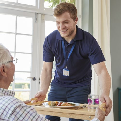 Male care worker serving dinner to a senior man at his home