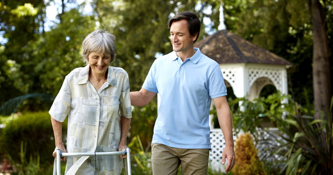 Male caretaker assisting senior woman in using walker at park